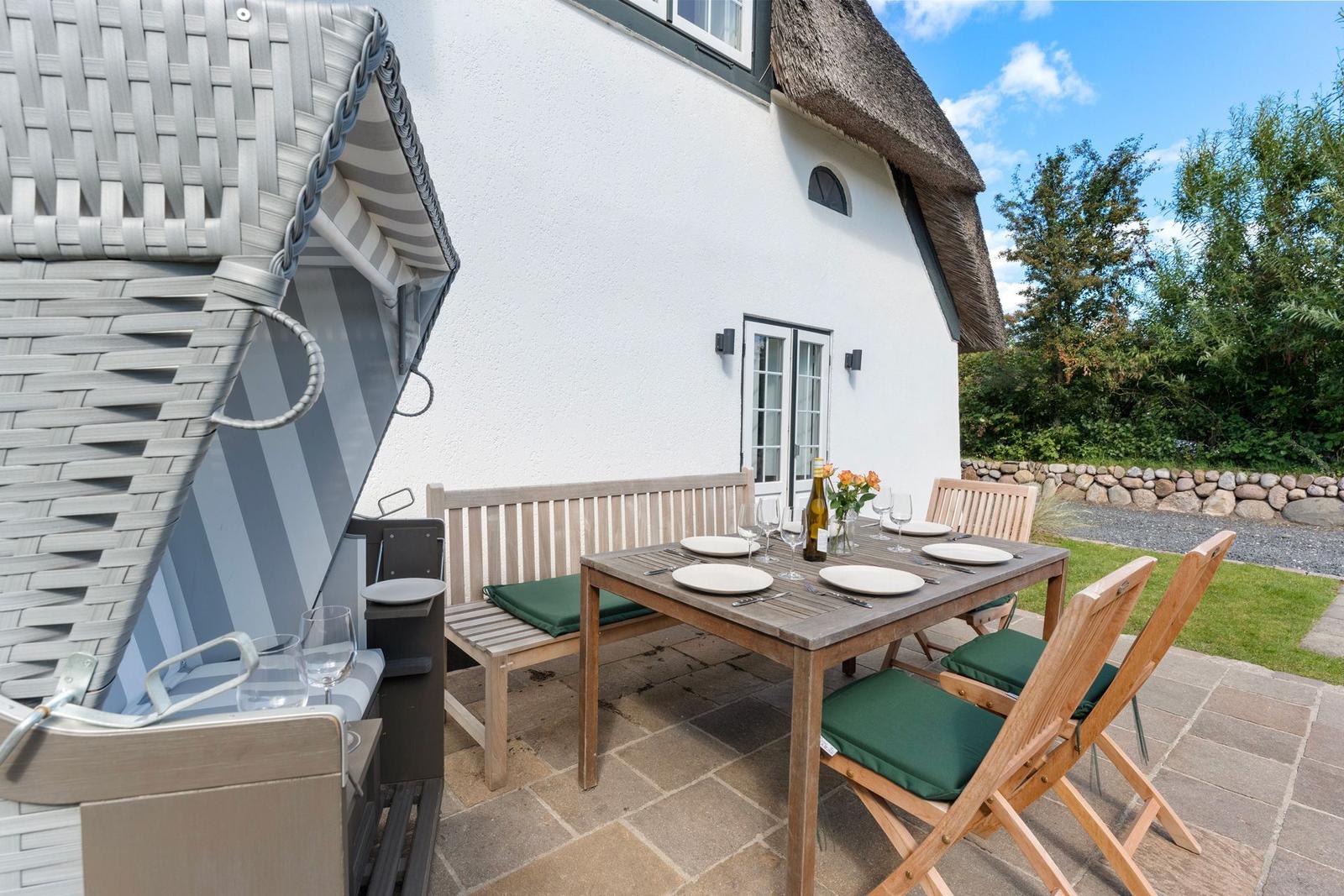 Terrasse mit Tisch, Stühlen und Sonnenschutz vor einem Haus mit Strohdach.