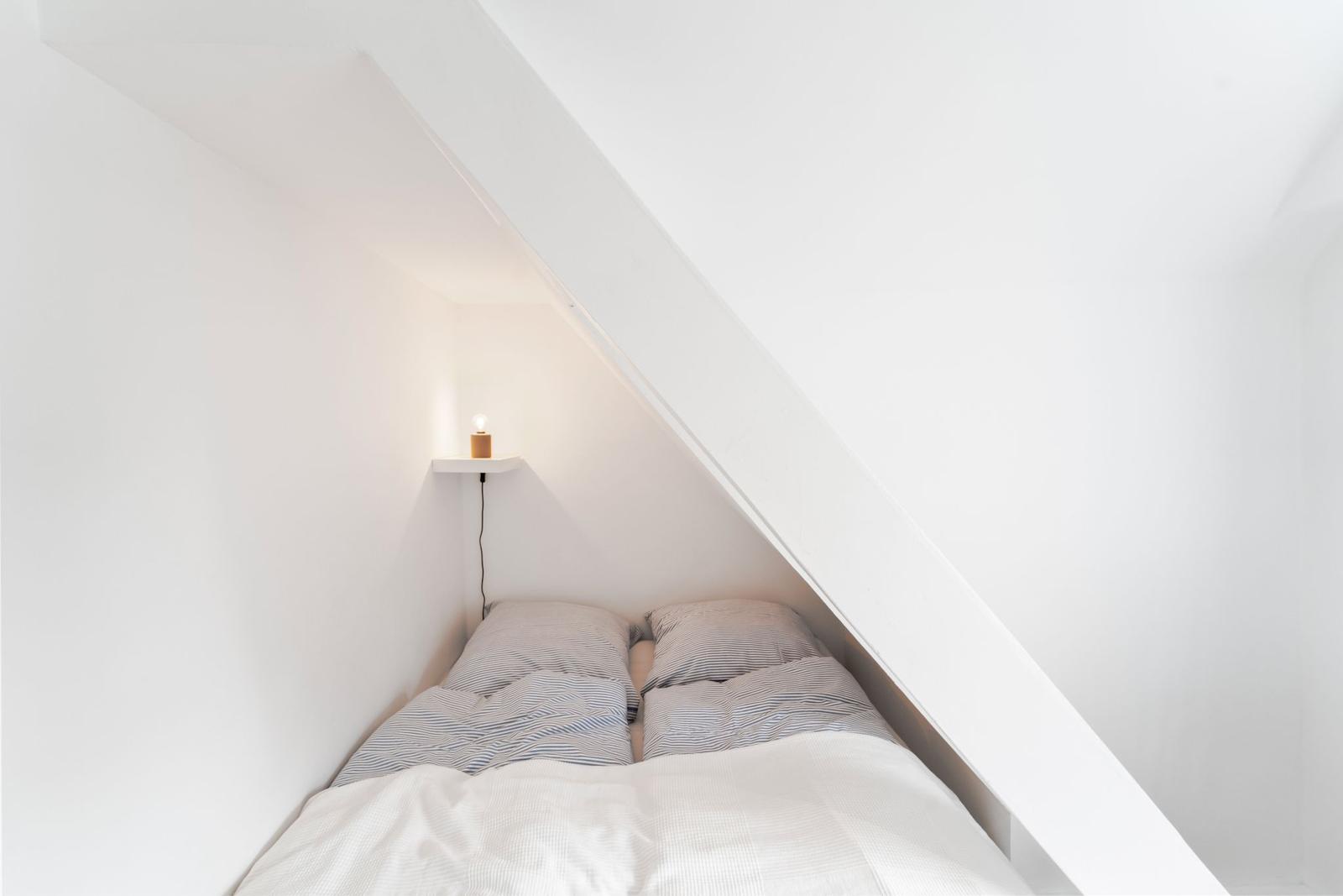 Doppelbett unter Dachschräge mit Bettwäsche und Wandlampe