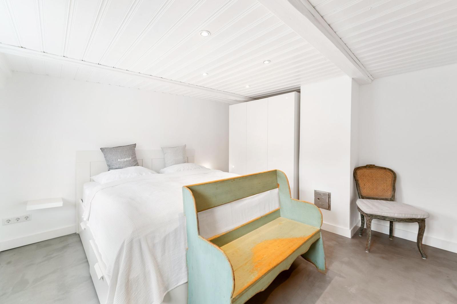 Schlafzimmer mit Bett, Bänke und Stuhl. Weiße Wände und Decke.