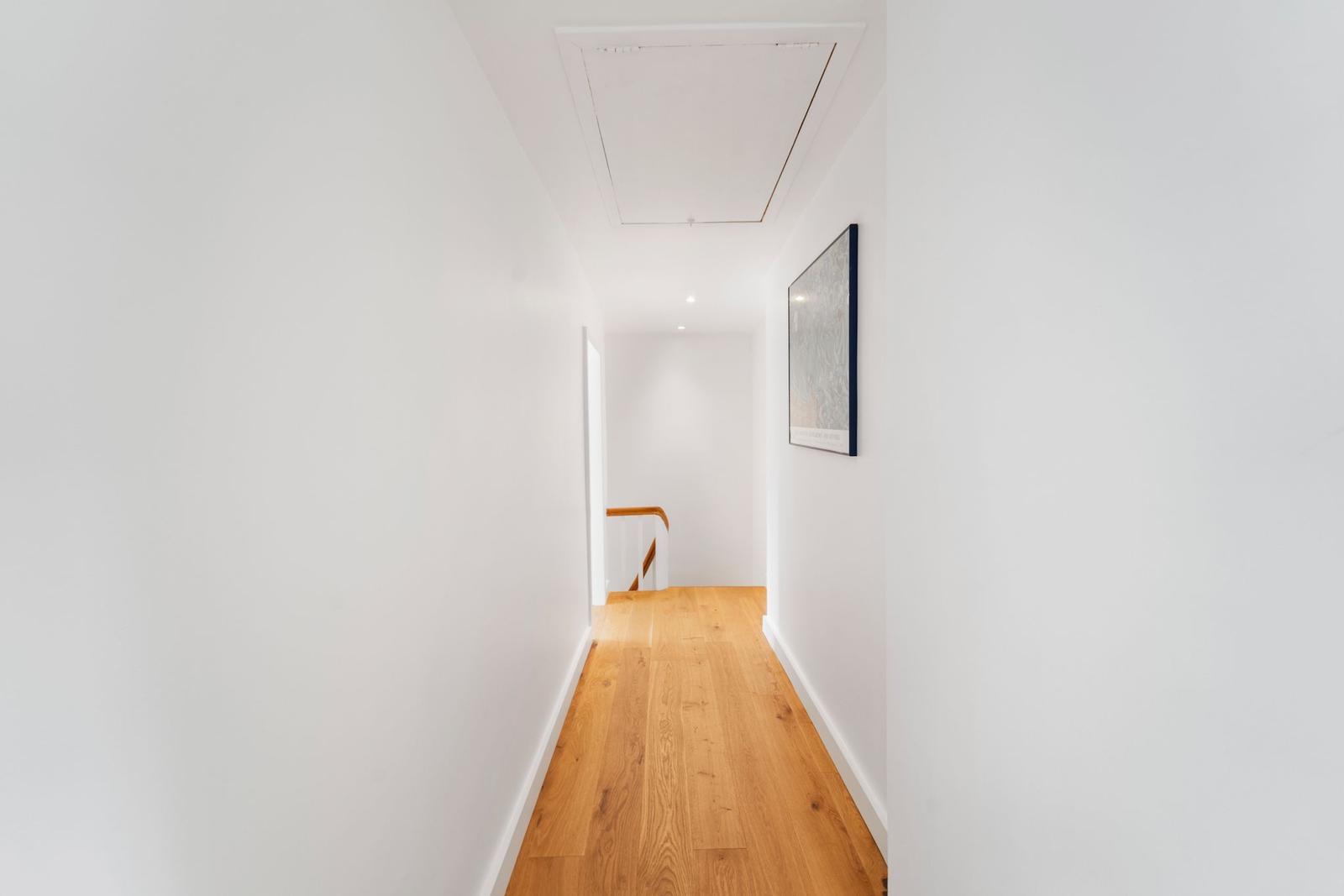 Flur mit Holzboden und weißer Wand, Bild an der Wand, Treppe im Hintergrund.