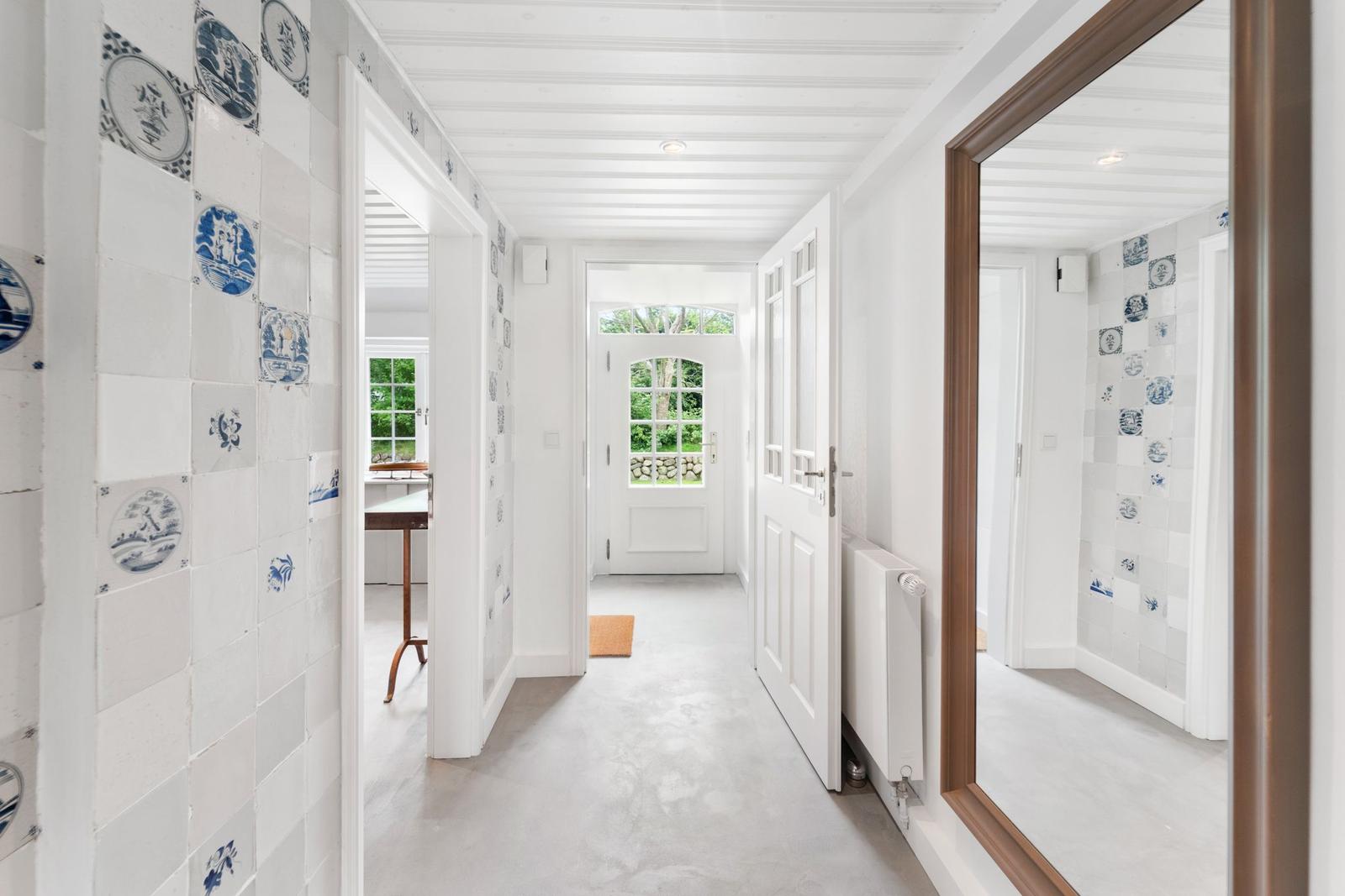 Flur mit blau-weißen Fliesen, weißer Tür und Spiegel