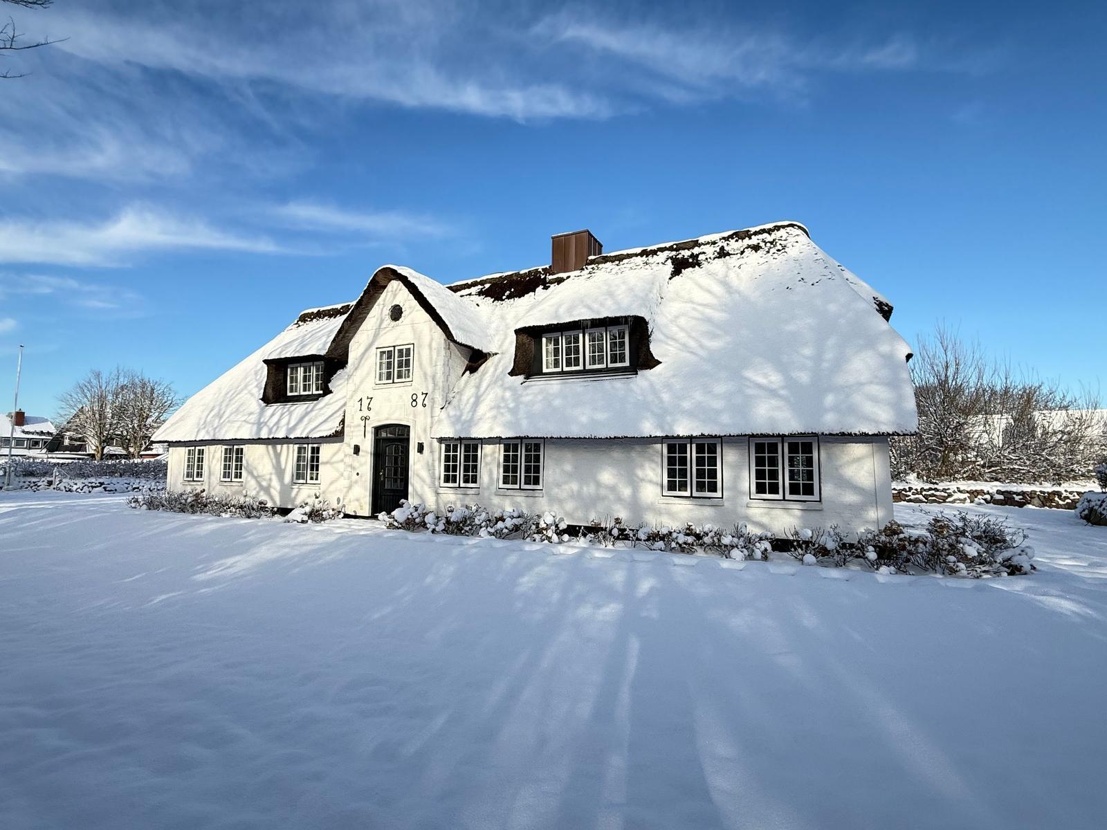 Schneebedecktes Haus mit strohgedecktem Dach und weißen Wänden.