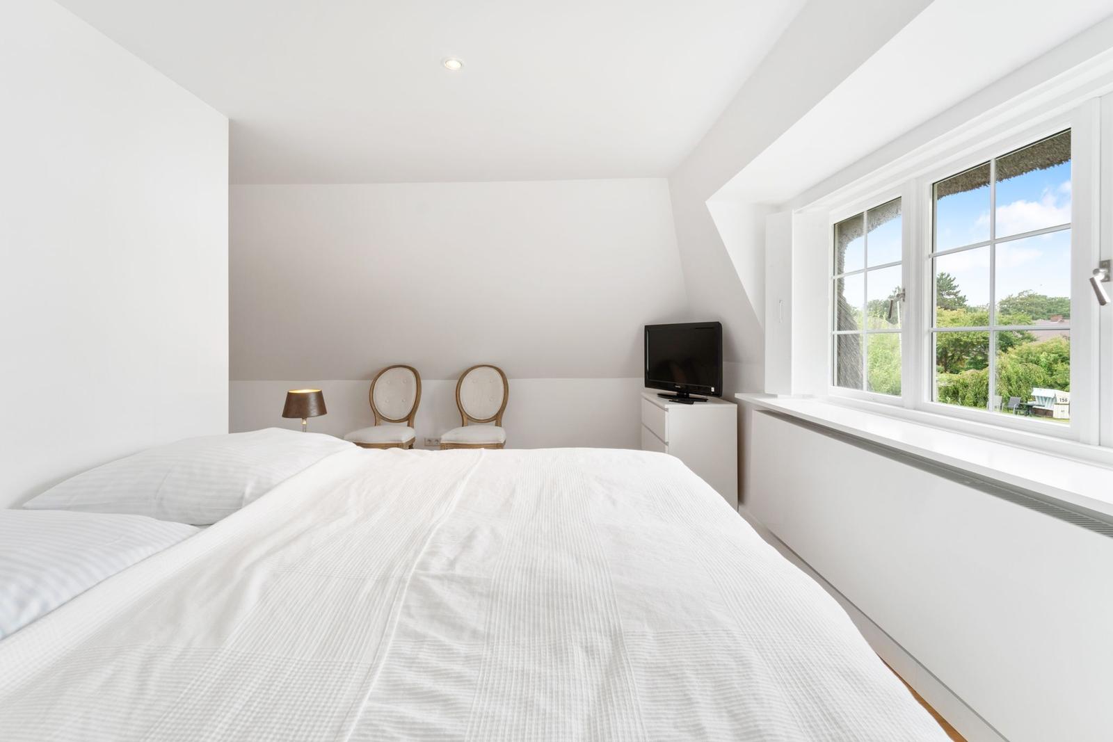 Schlafzimmer mit Bett, TV und Fensterblick auf Garten