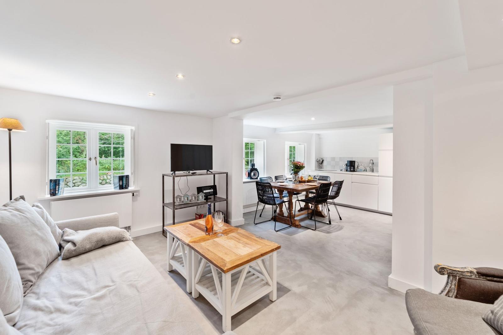 Wohn- und Essbereich mit TV, Tisch und Sofa. Küche im Hintergrund.