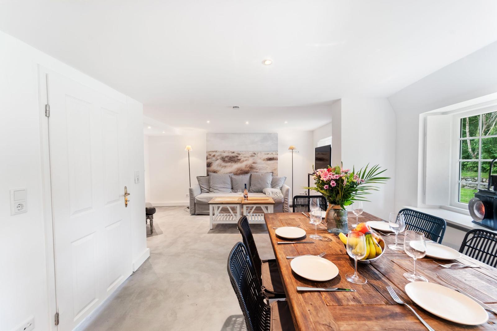 Esszimmer mit Holztisch und Stühlen. Im Hintergrund Wohnbereich mit Sofa und Wandbild.