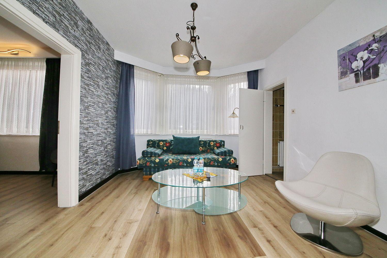 Wohnzimmer mit Sofa, Glas-Tisch und moderner Sitzgelegenheit. Blick auf angrenzende Räume.