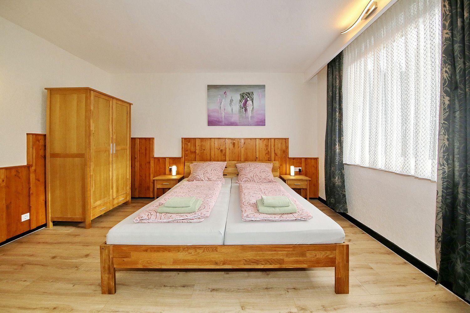 Schlafzimmer mit Doppelbett, Holzmöbel und Fenster mit Vorhängen.