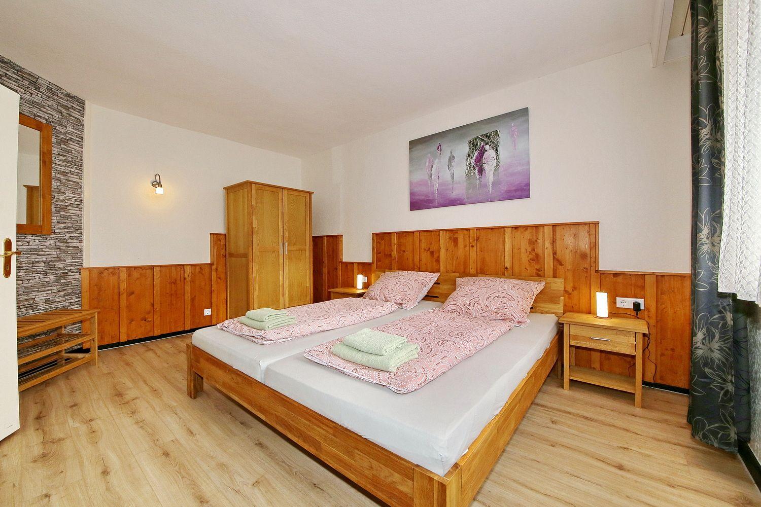 Schlafzimmer mit Holzbett, Nachttischen und Kleiderschrank. Wandbild und Holzvertäfelung.