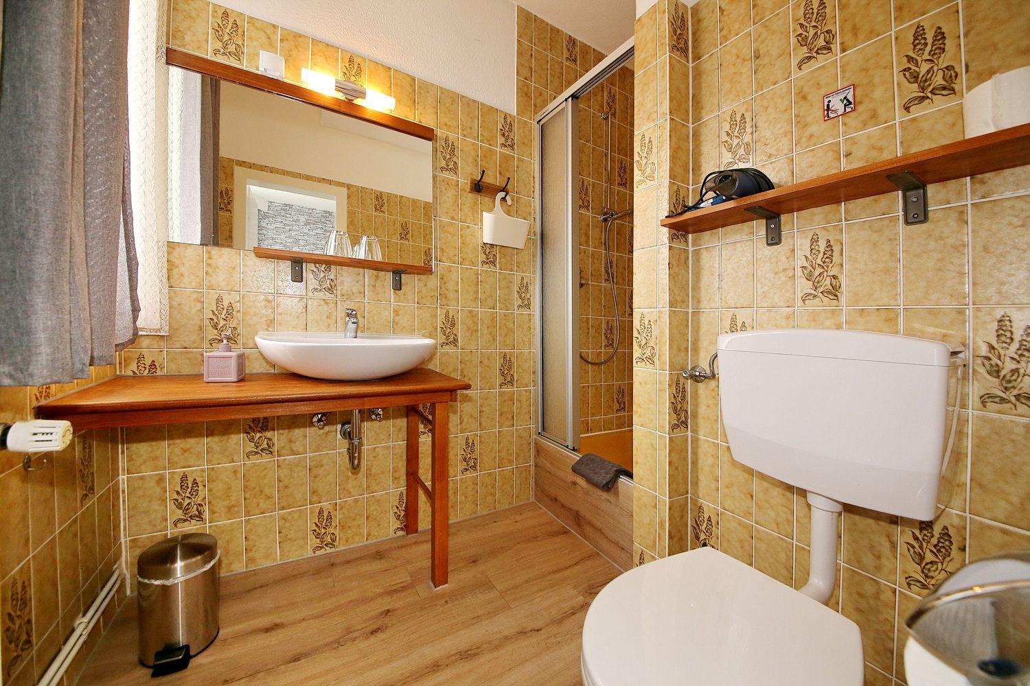 Badezimmer mit Dusche, Waschbecken und Toilette. Fliesenwand und Holzboden.