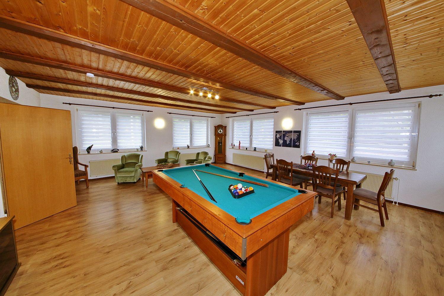 Raum mit Billardtisch, Essbereich und Sitzgelegenheiten unter Holzdecke.