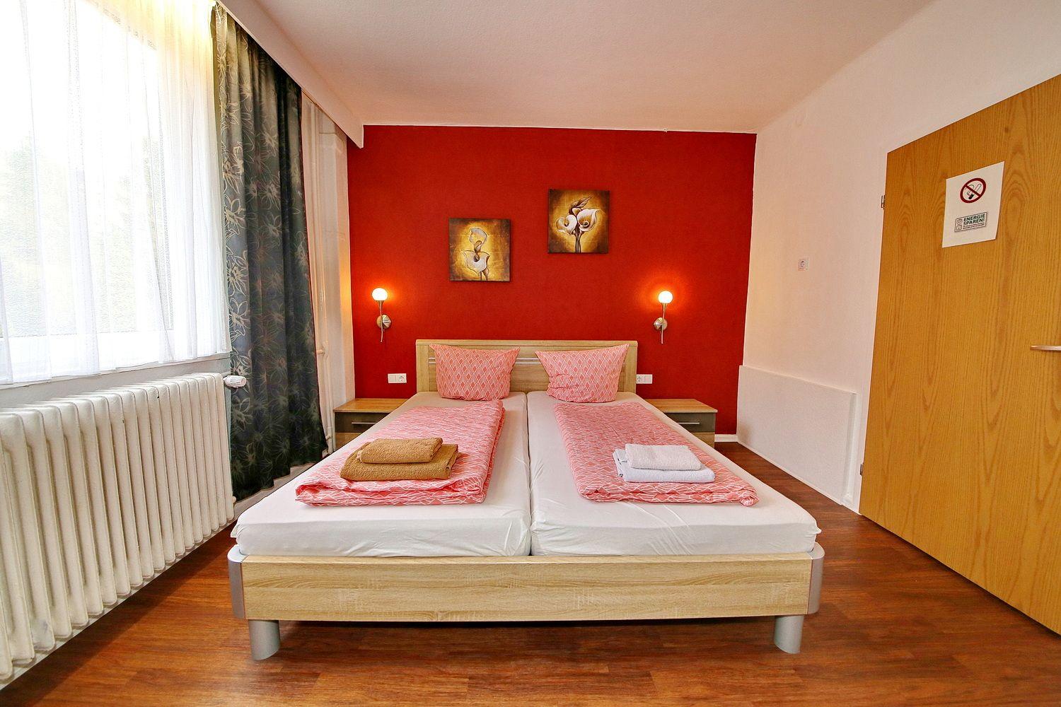 Schlafzimmer mit Doppelbett, roter Wand und Fenster mit Vorhängen.