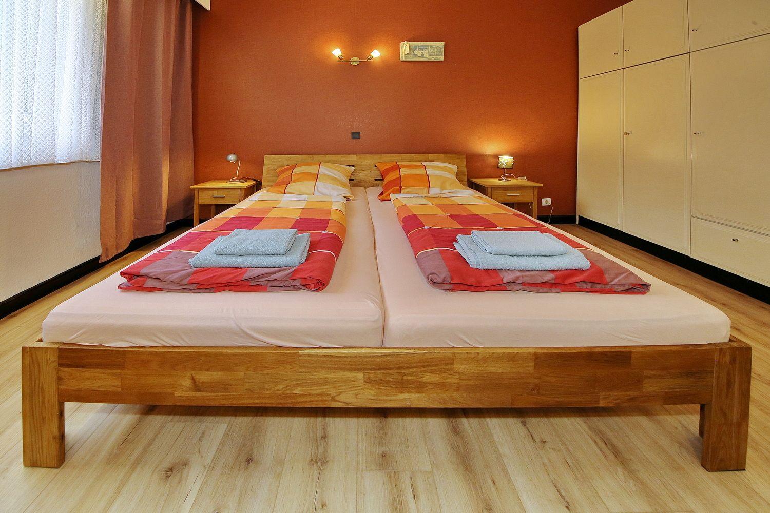 Zwei Betten mit bunten Bettwäsche und Holzrahmen. Wandbeleuchtung und Kleiderschrank.