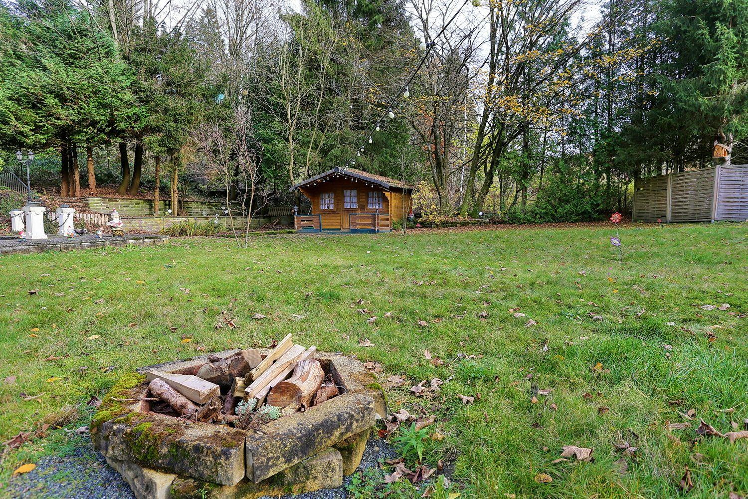 Holzhütte im Wald mit Grillplatz und Grünfläche.