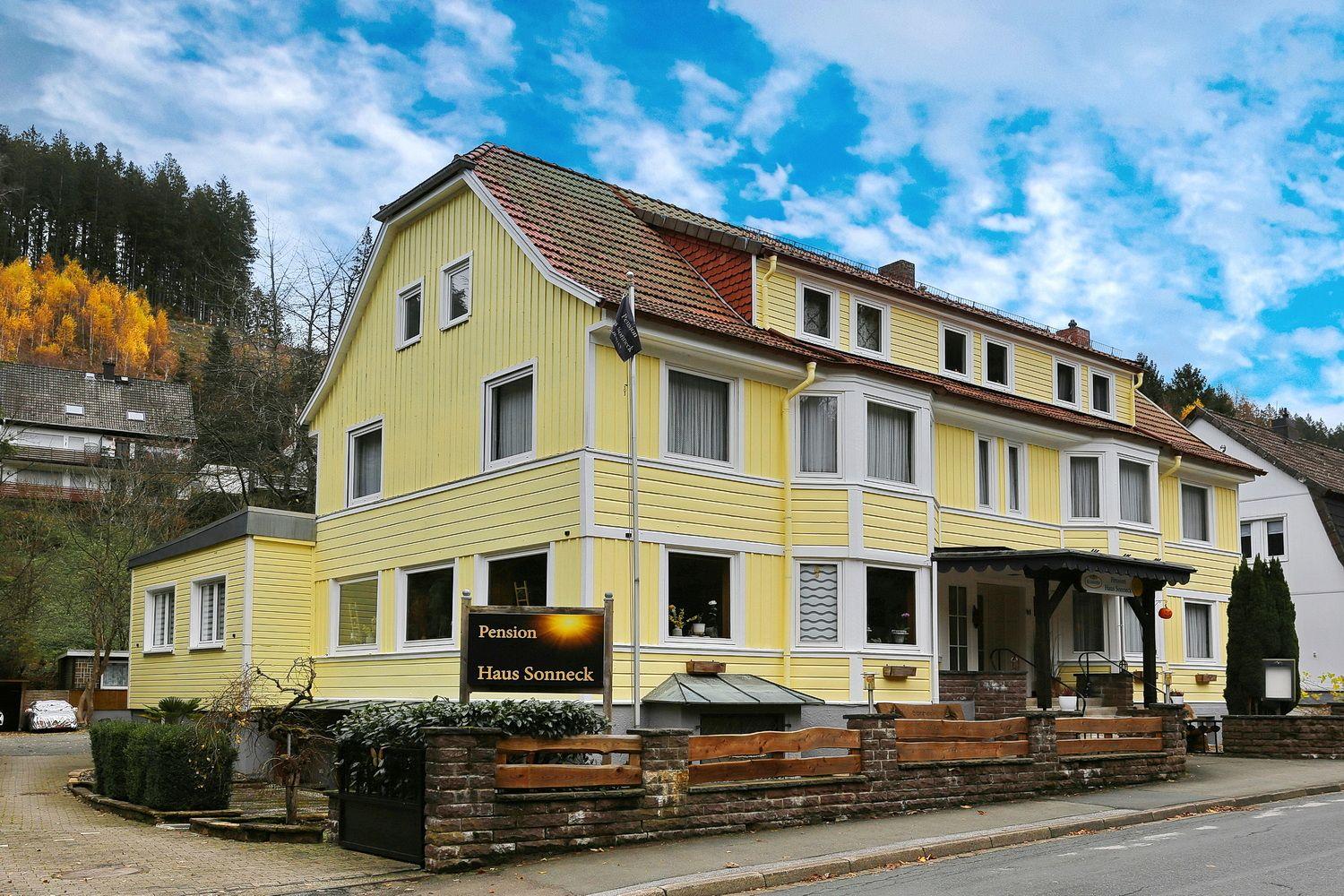 Gelbes Haus mit Satteldach und Balkon. Schild: Pension Haus Sonneck.