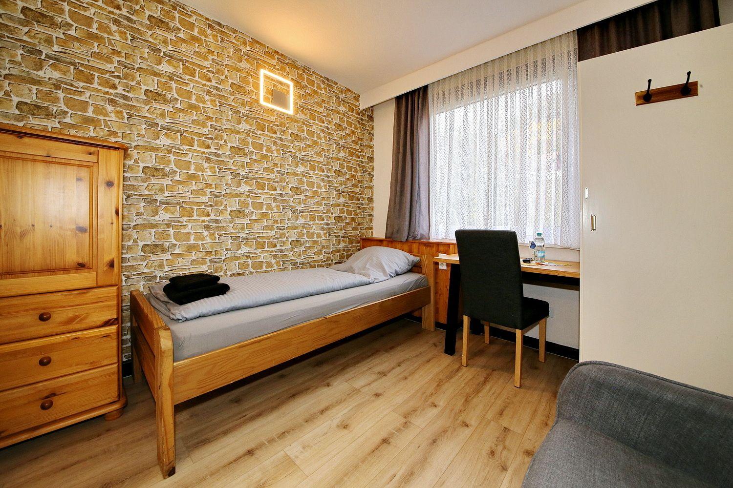 Ein Schlafzimmer mit Holzbett, Schrank und Schreibtisch an Fenster