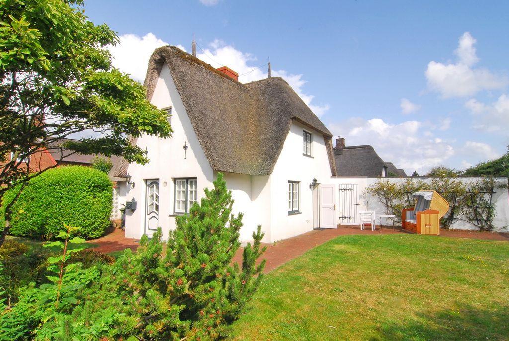 Weiße Hütte mit Strohdach, Garten und Liegestühle.