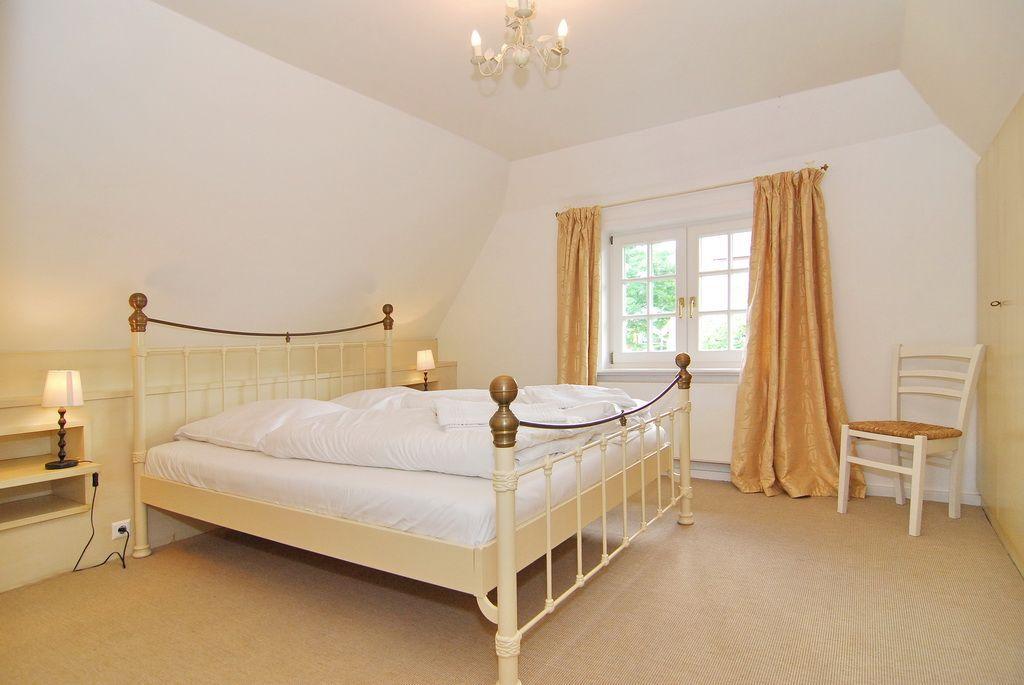 Schlafzimmer mit Bett, Fenster, Vorhängen und Stuhl.