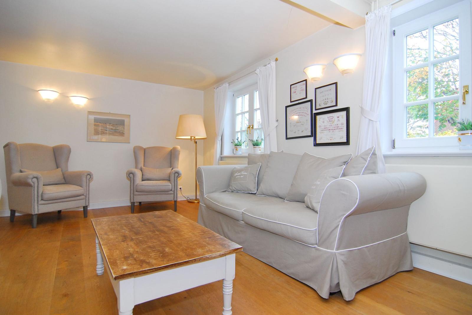 Wohnzimmer mit Sofa, zwei Sesseln, Tisch und Fenstern.