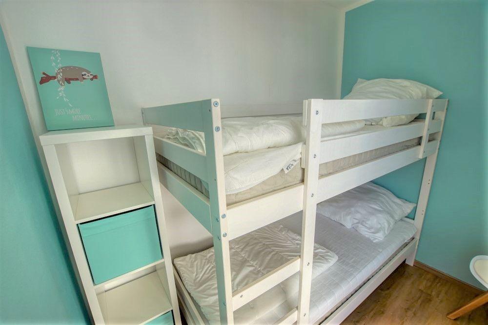 Zimmer mit Doppelstockbett und weißen Matratzen. An der Wand hängt ein Bild.