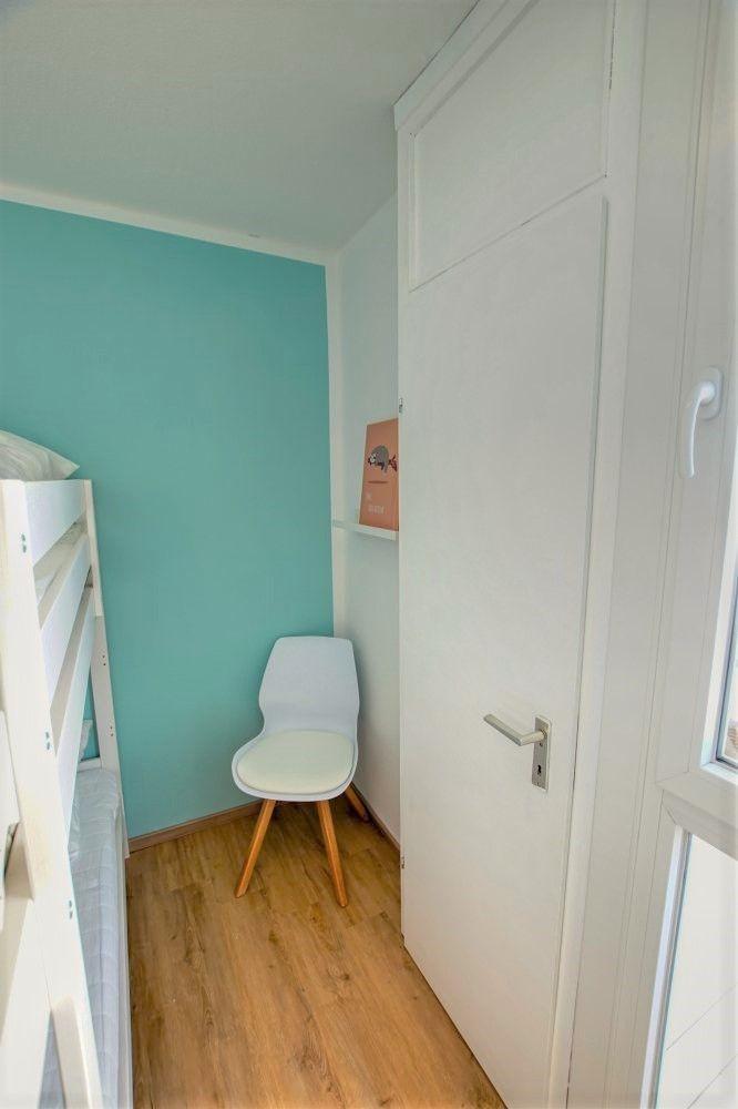 Zimmer mit Doppelstockbett, Stuhl und Tür. Wandfarbe Türkis.