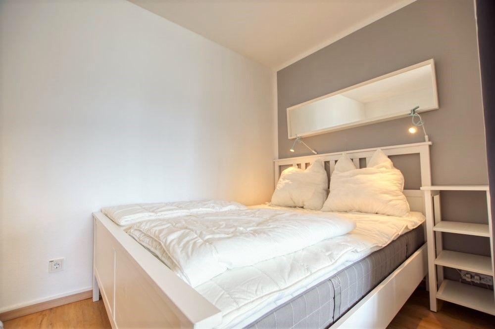 Schlafzimmer mit weißem Bett, Spiegelschrank und Nachttisch.