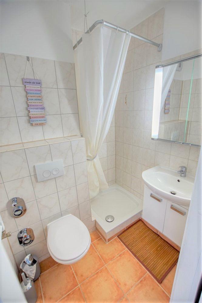 Badezimmer mit Dusche, Waschbecken und Toilette. Fliesenboden und Spiegelschrank.