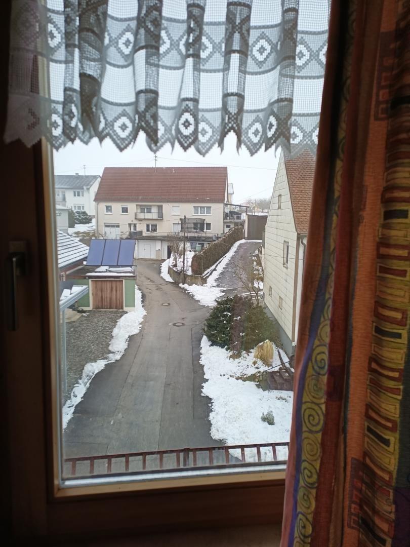 Aus dem Fenster blickt man auf eine schneebedeckte Straße mit Häusern.