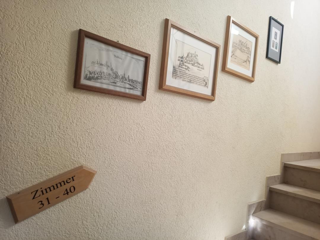 Wand mit Bildern und Schild für Zimmer 31 bis 40 neben Treppe