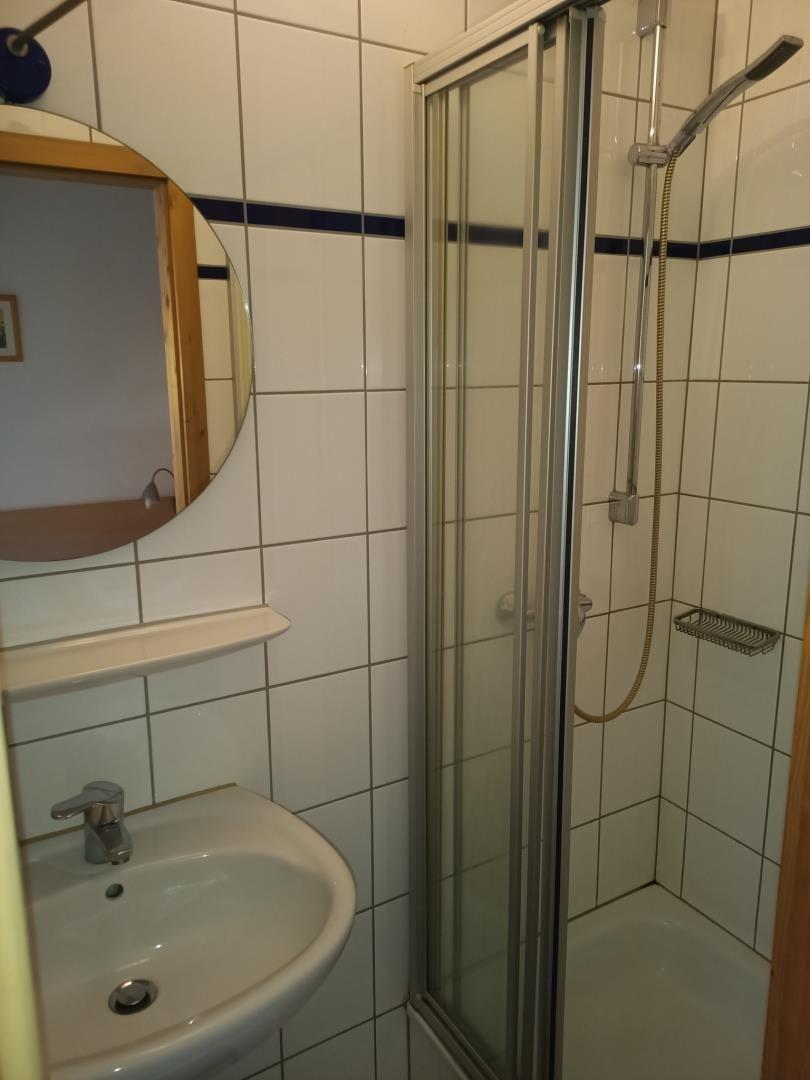 Bad mit Dusche, Waschbecken und runden Spiegel
