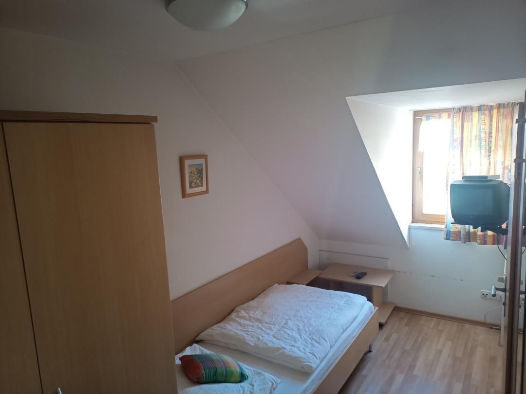 Schlafzimmer mit Dachschrägen, Bett, Kleiderschrank und Fenster.