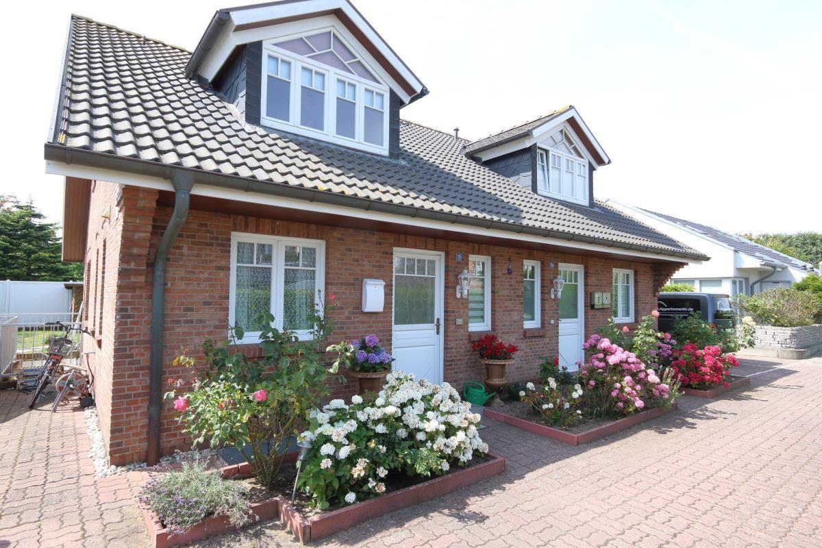 Rotes Backsteinhaus mit Dachgauben und Blumenbeeten vor der Tür.