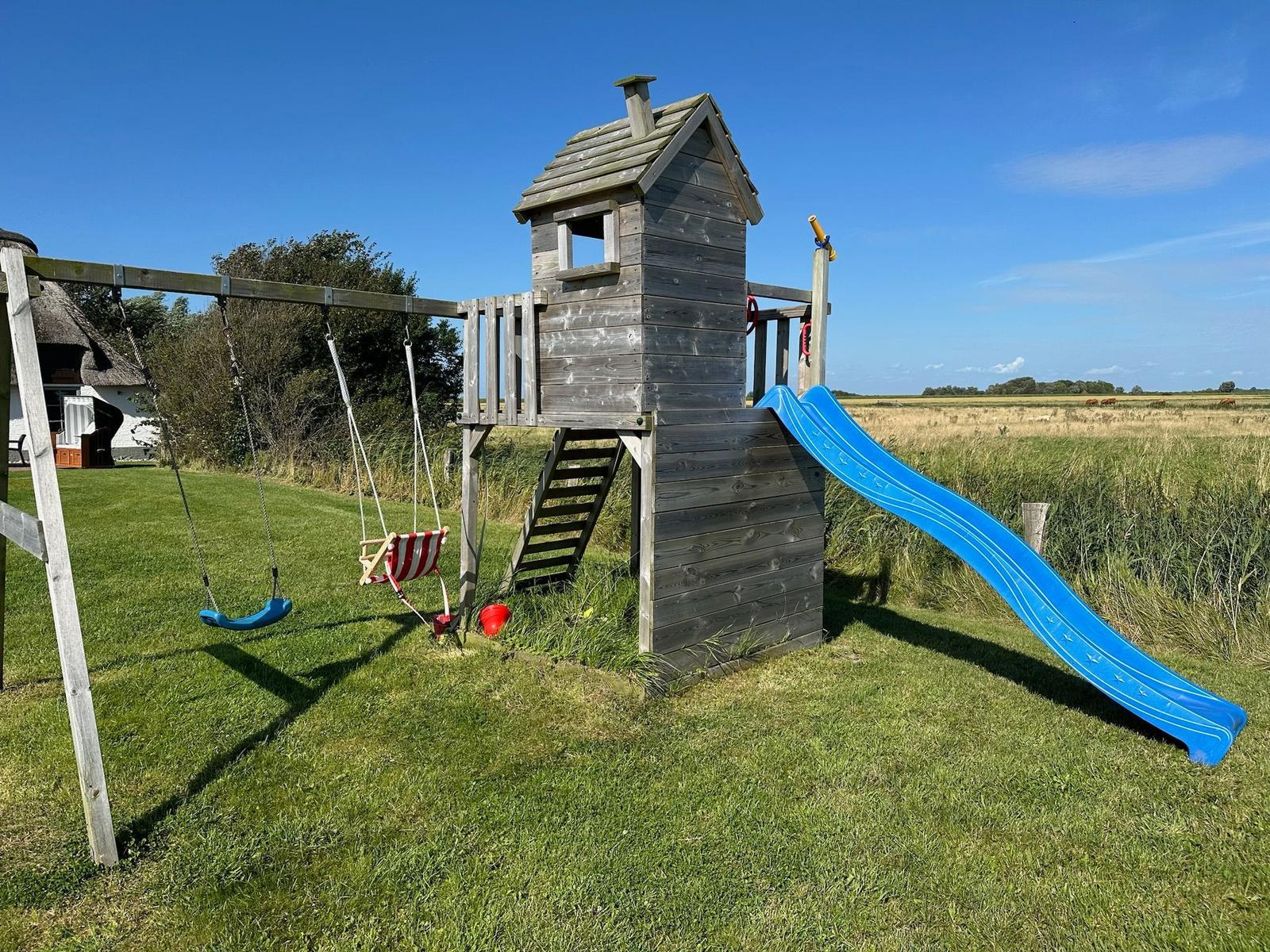 Holzspielplatz mit Rutsche und Schaukel auf grünem Rasen.