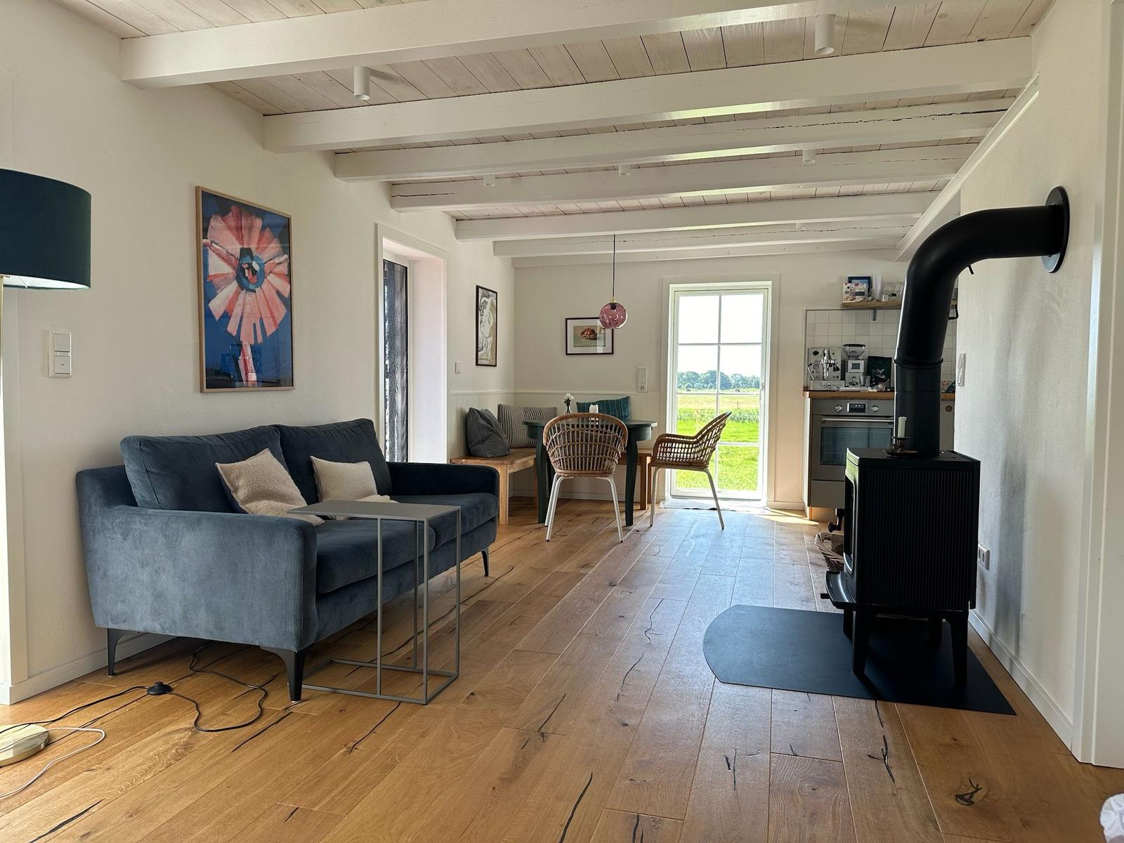 Wohnzimmer mit Sofa, Esstisch und Kaminofen. Holzboden und weiße Wände.