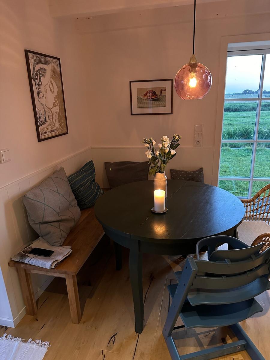 Runde Tisch mit Kerze und Blumen, Sitzbank mit Kissen, Fensterblick auf Grünland.