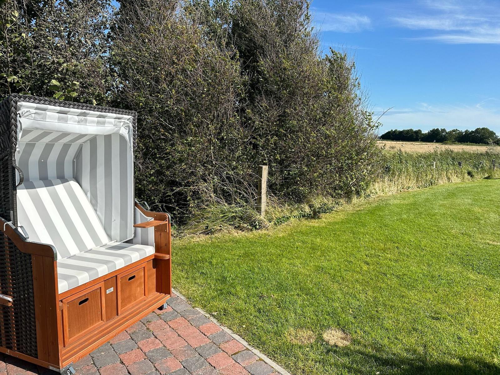 Strandkörbe auf gepflastertem Bereich mit Blick auf Gras und Feld.