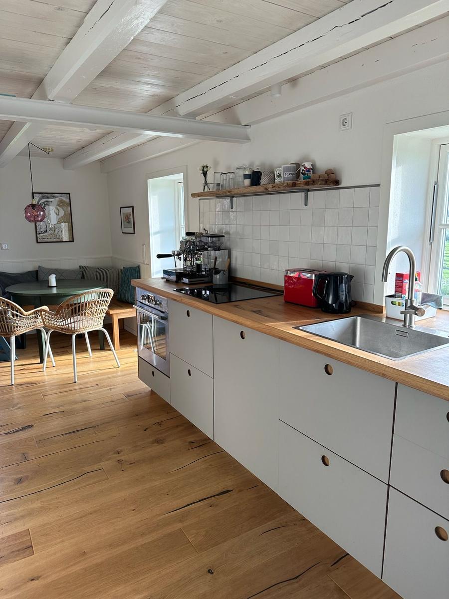 Küche mit Holzwerkstoffe und Edelstahlspüle. Essbereich mit runden Tisch und Stühlen.