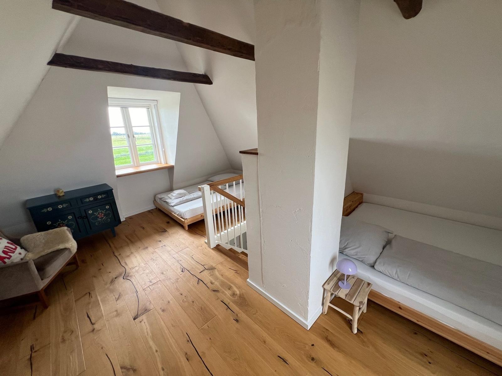 Zimmer mit Holzboden, Fenster und zwei Betten unter Dachschrägen.
