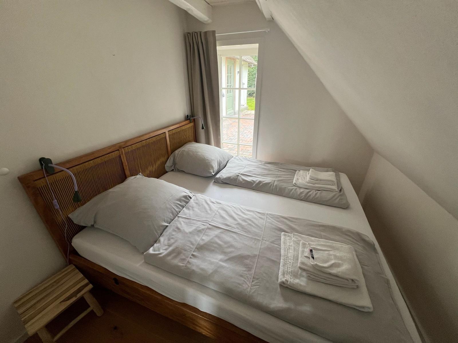 Schlafzimmer mit Doppelbett, Fenster und Holzgestell.