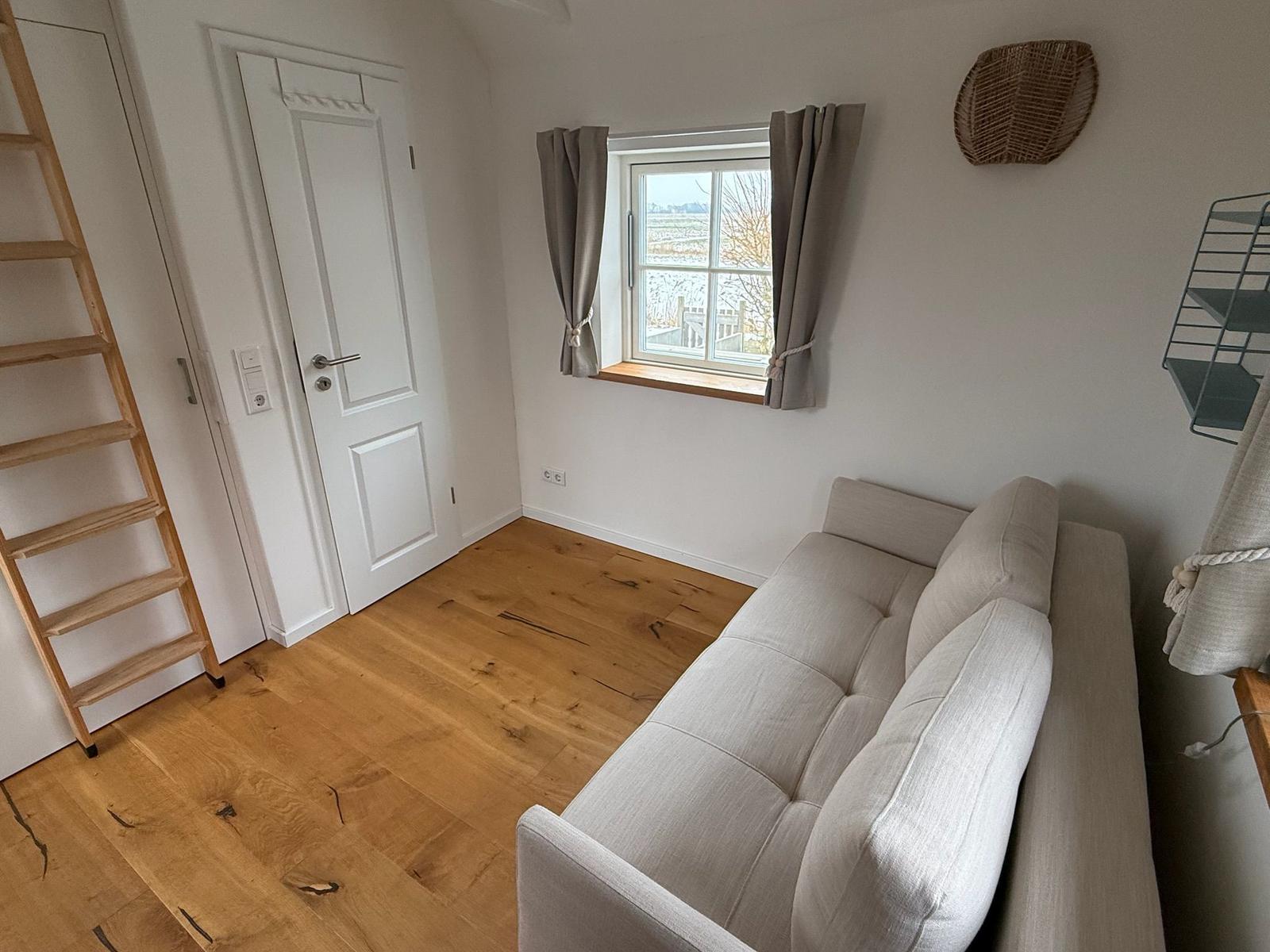 Wohnraum mit Sofa, Holzboden und Fenster mit Blick auf Landschaft.