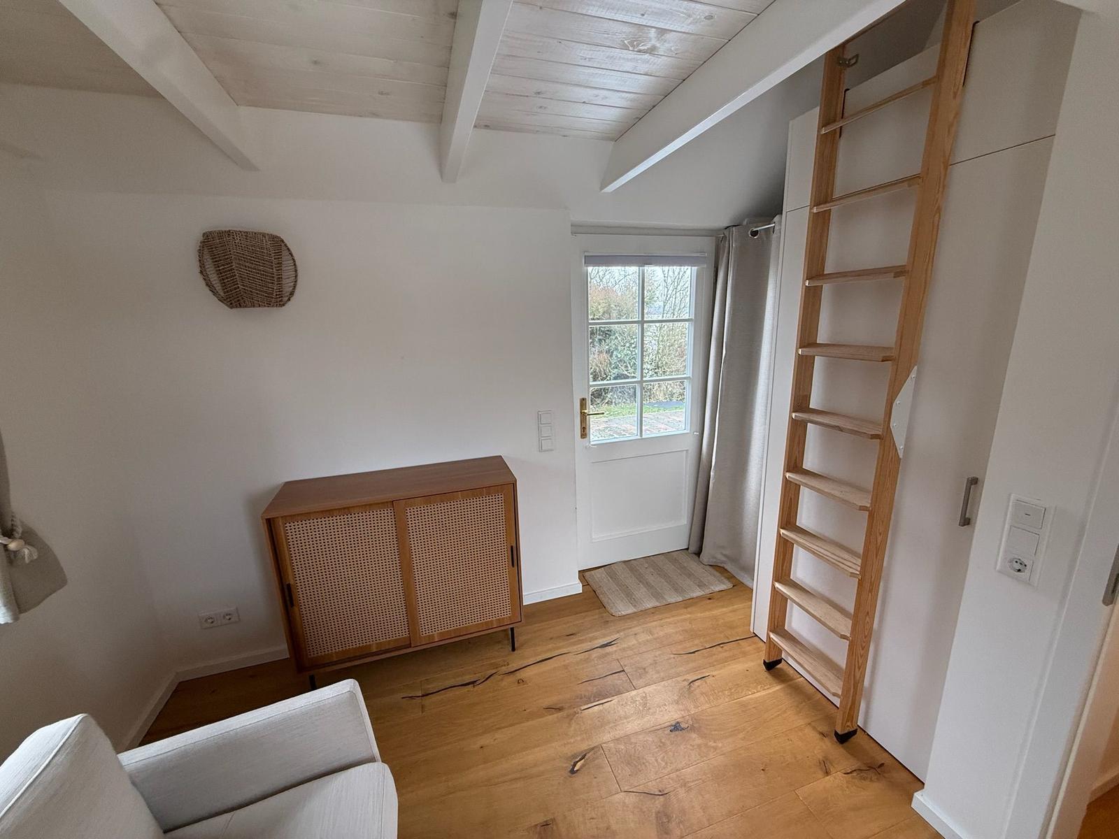 Raum mit Holzboden, Treppe und Fenster zur Außenseite.