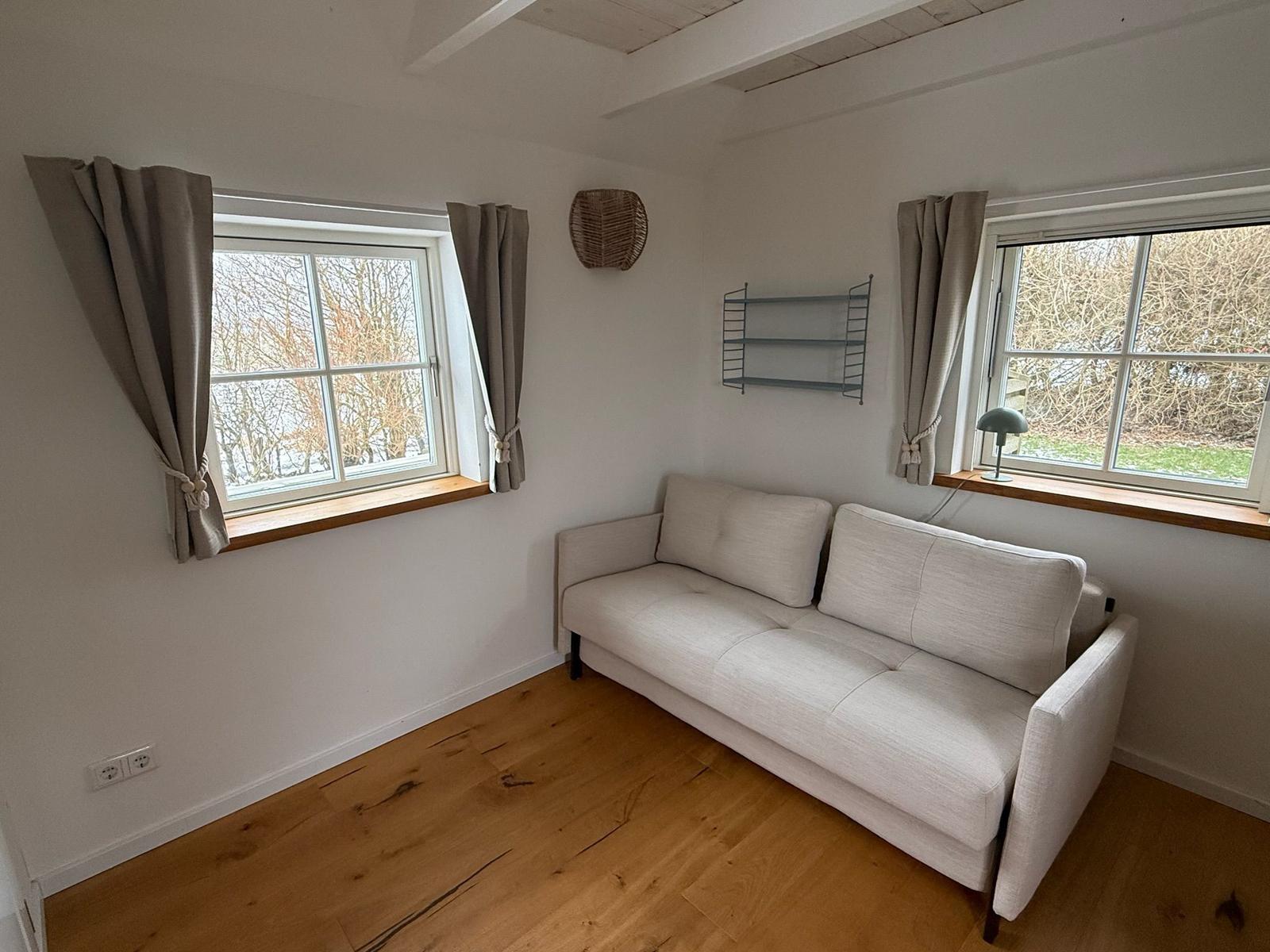 Ein Raum mit Sofa, zwei Fenstern und Holzboden.