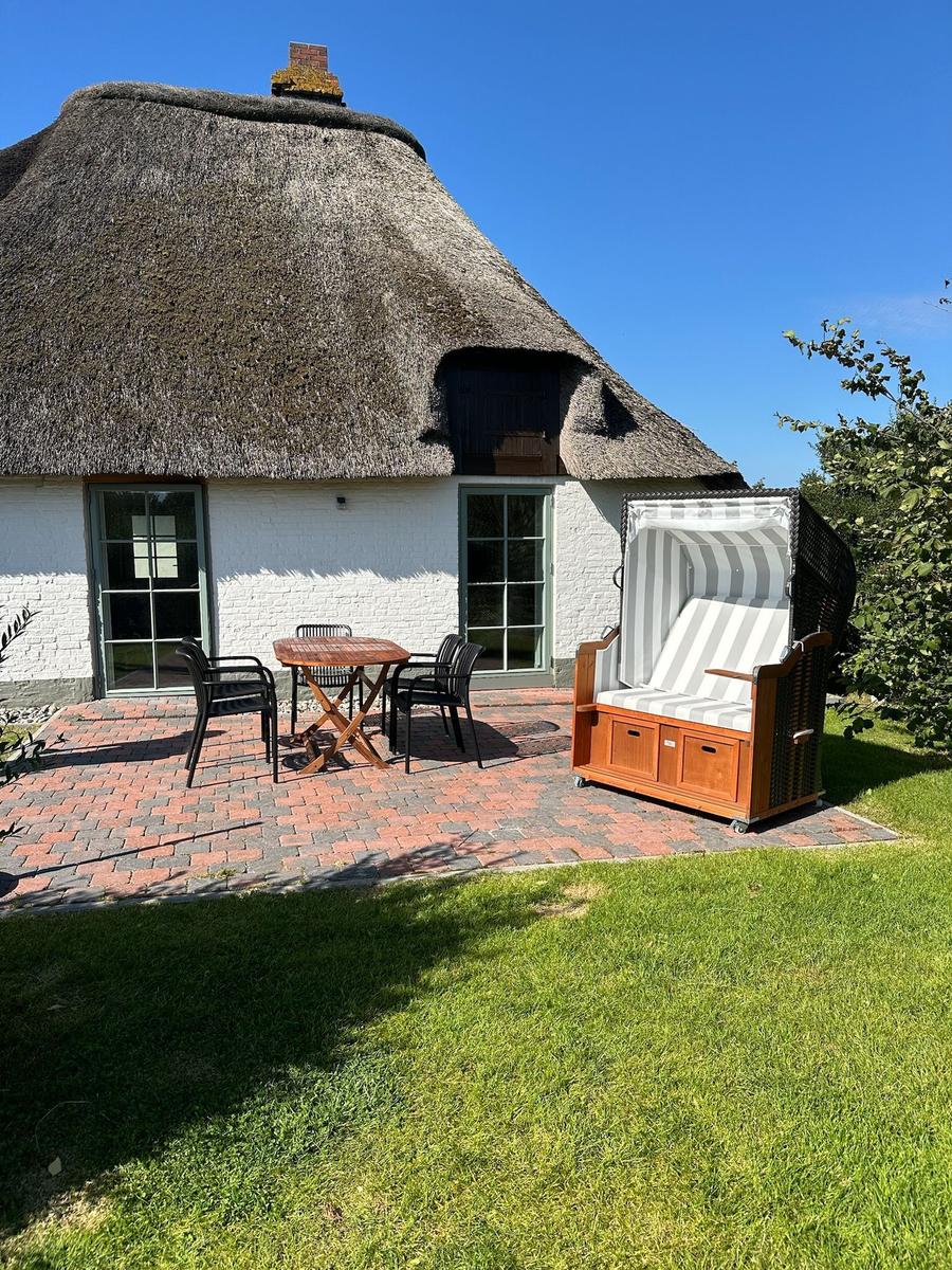 Haus mit Strohdach, Terrasse mit Tisch, Stühlen und Strandkorb.