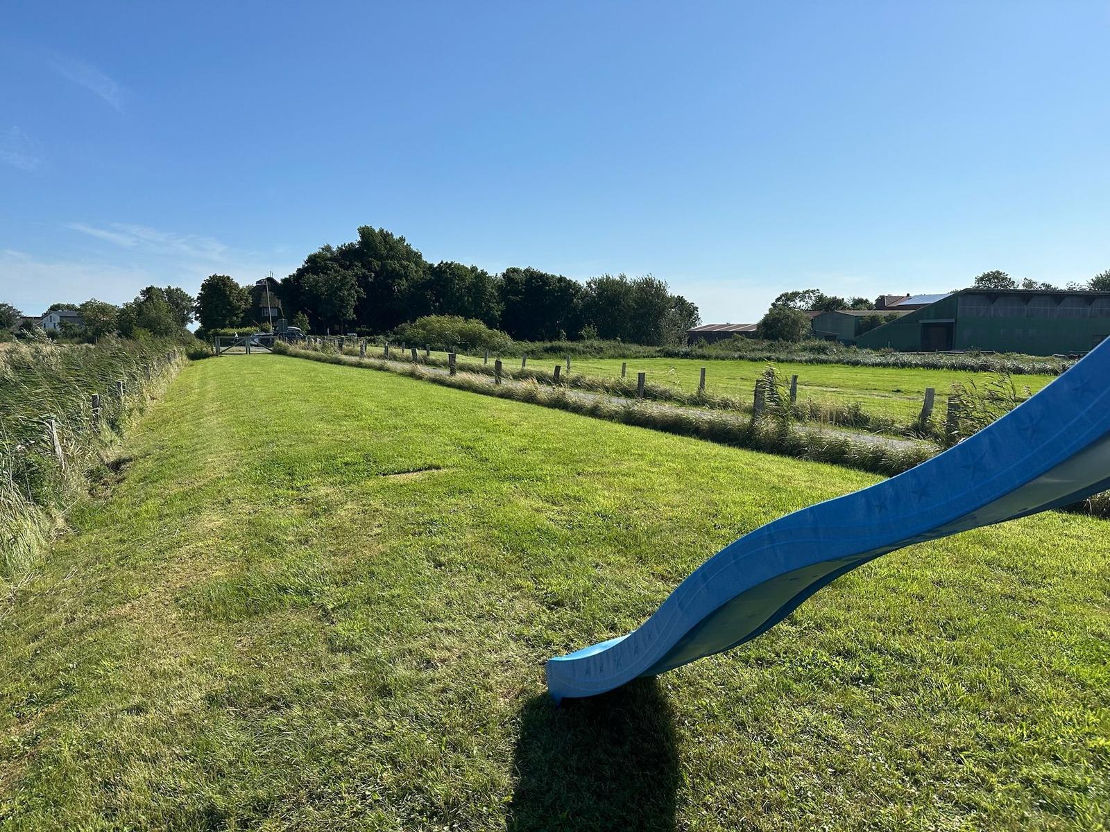 Blauer Rutsche im grünen Garten mit Blick auf Felder und Gebäude.