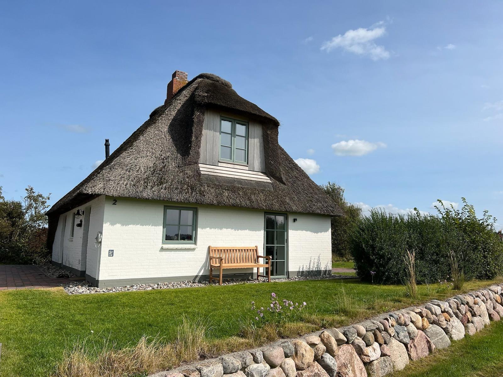Haus mit Strohdach, Holzbank und Steinmauer im Garten.