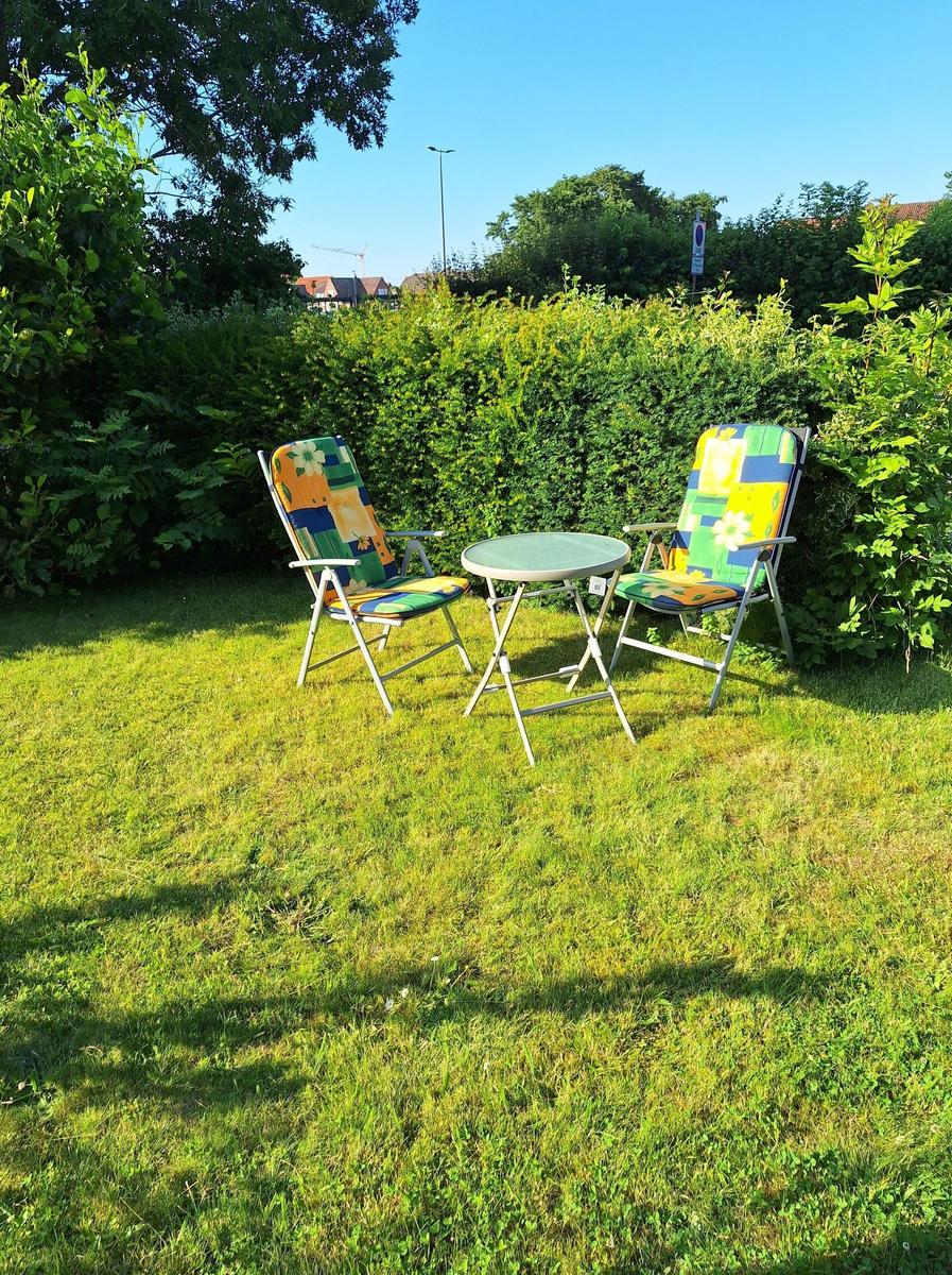 Two colorful garden chairs and a table are on the lawn.