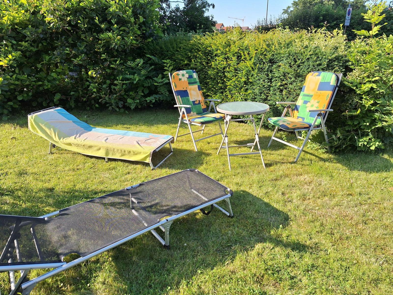 Garden with loungers, two chairs, and table. Background: green hedge.