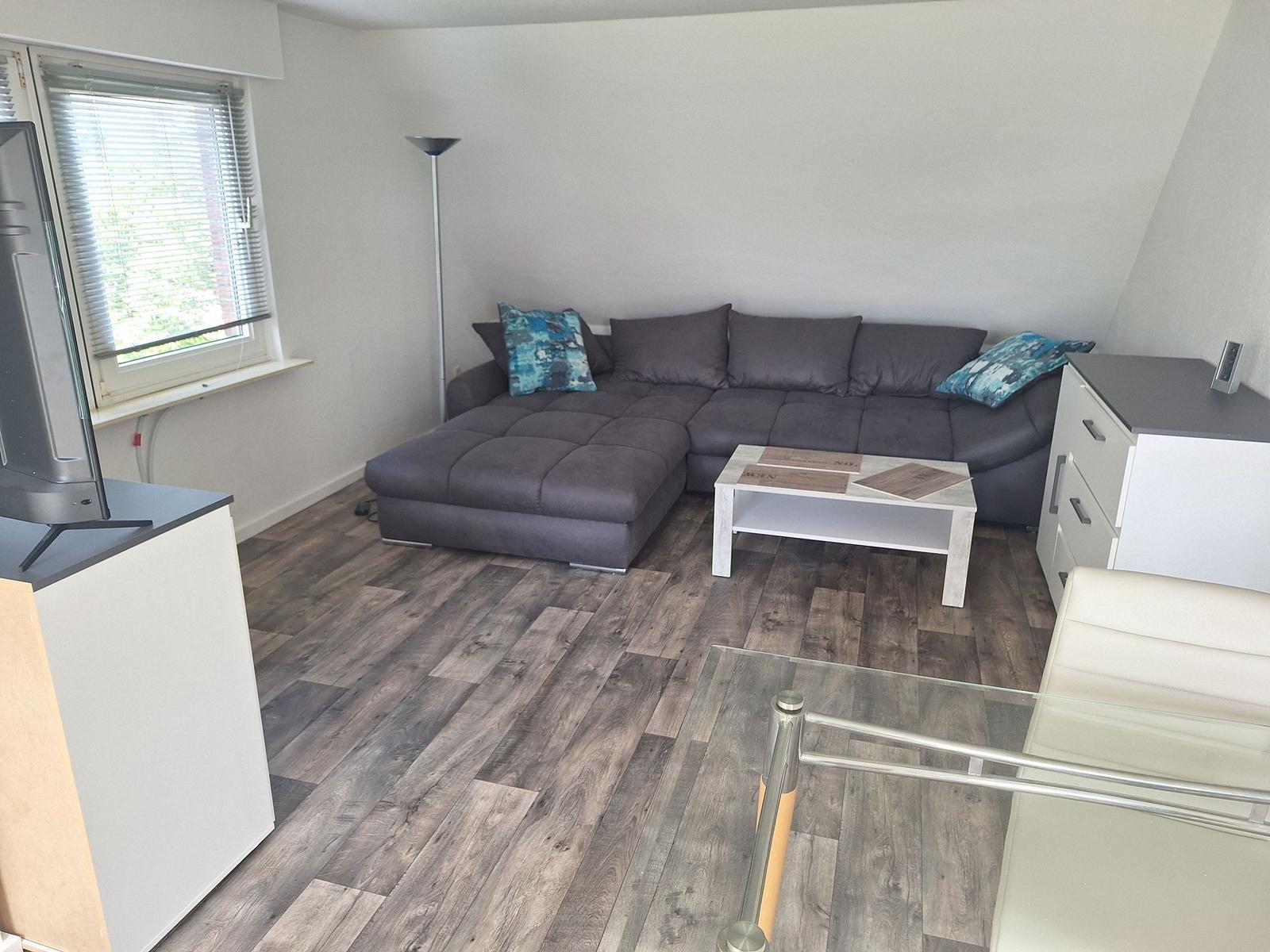 Living room with corner sofa, glass table, and wooden floor.