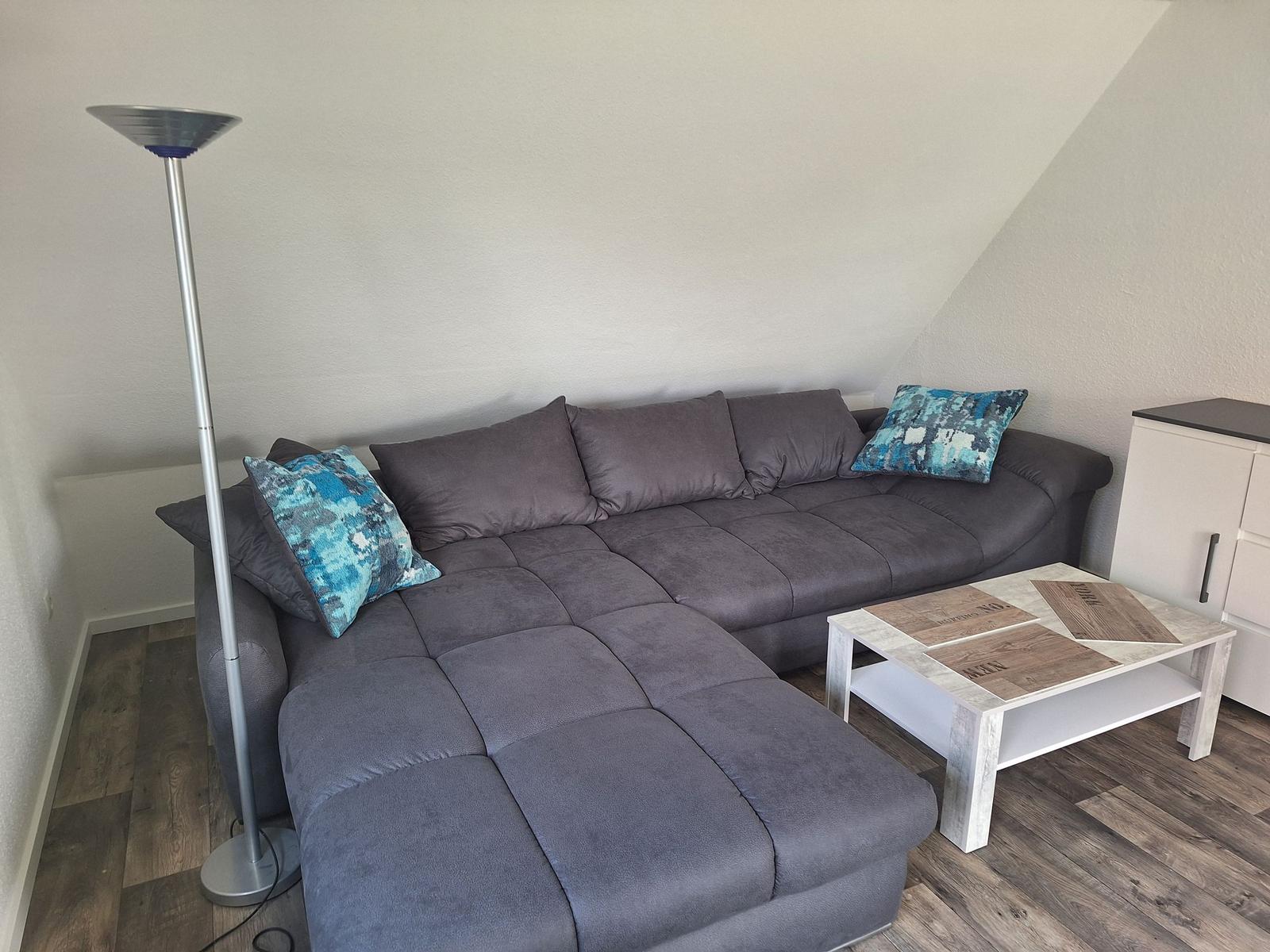 Gray corner with sofa, table, and floor lamp in attic room.
