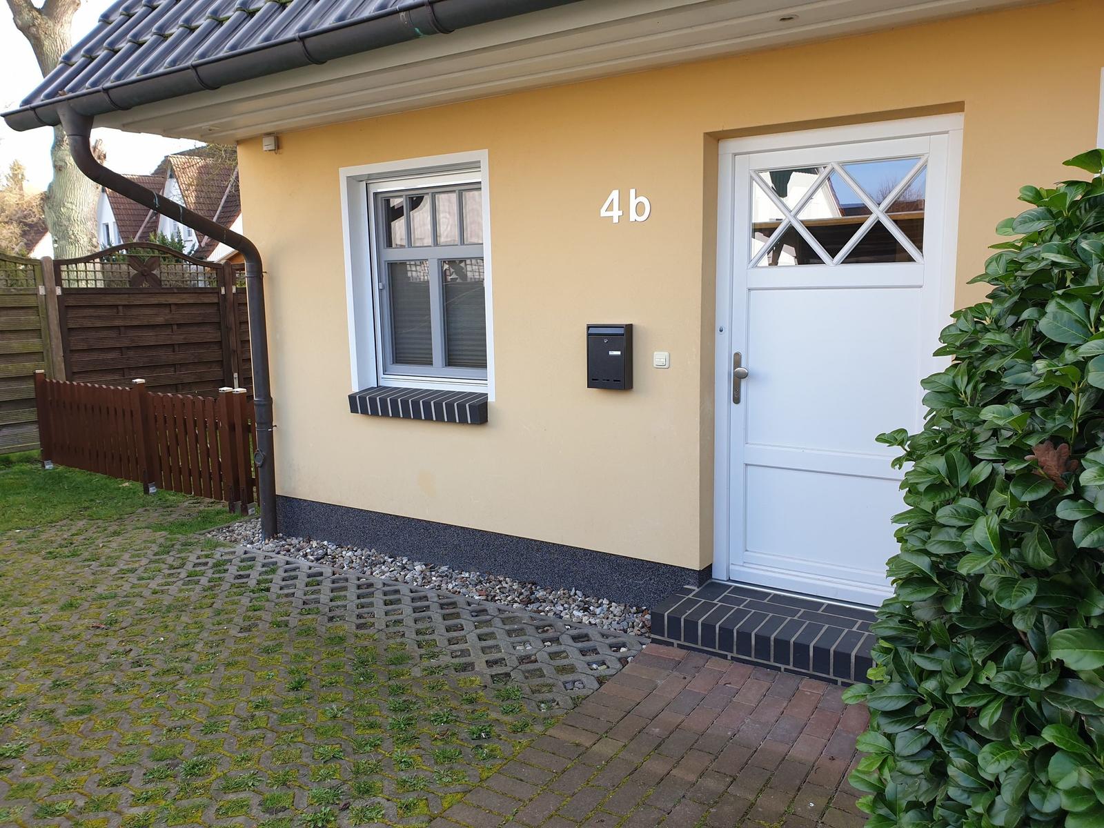 Haus mit gelber Fassade, weißer Tür und gepflastertem Vorgarten.
