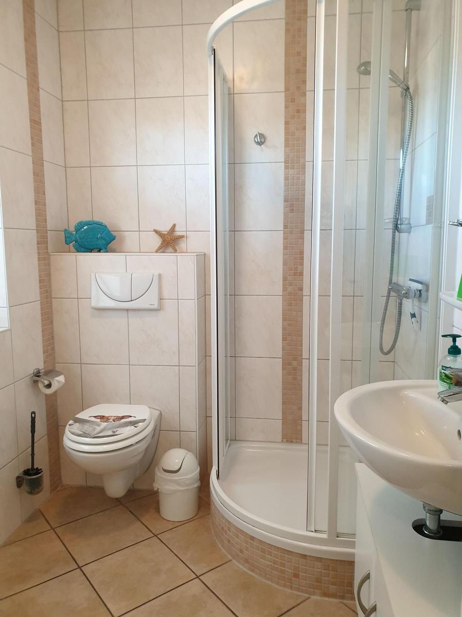 Badezimmer mit Dusche, Waschbecken und Toilette. Wand- und Bodenfliesen.